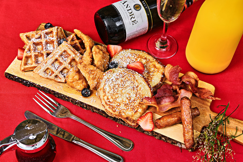 a variety of breakfast dishes are arranged on a board – from waffles and pancakes to savory sausage